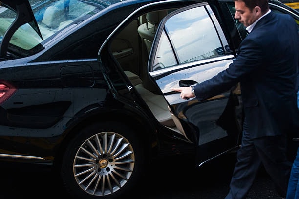 A chauffeur waiting for the client to board the car in a corporate limo.